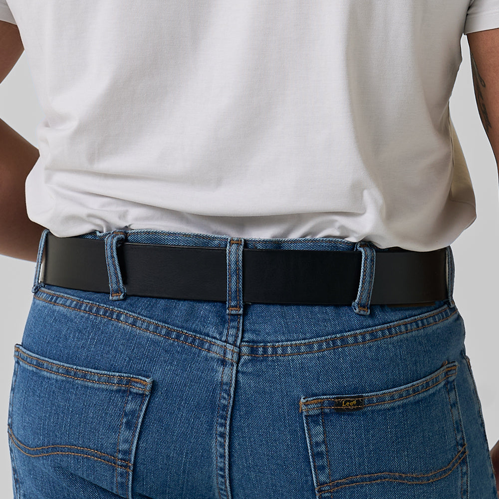 A person wearing a white t-shirt tucked into blue jeans is shown from the back at waist level, featuring The Enforcer concealed carry belt by Hanks Belts.