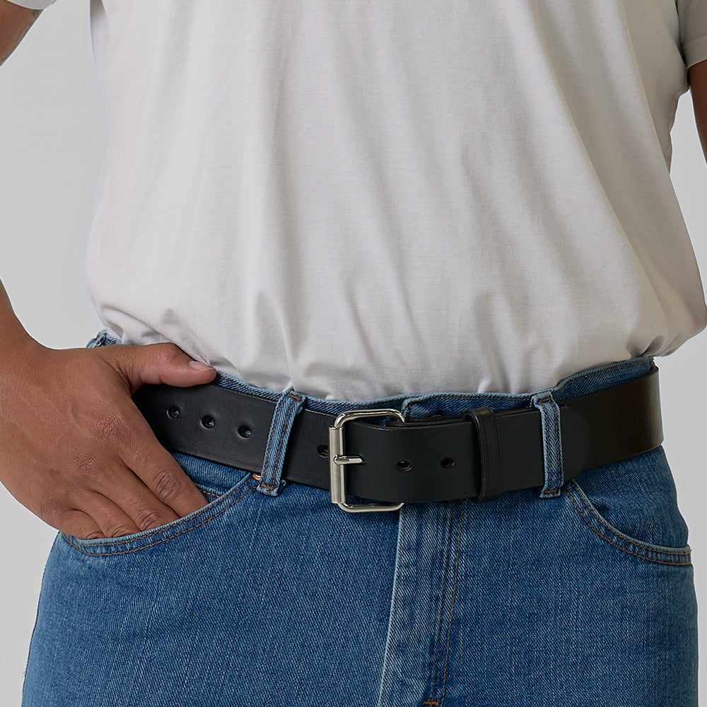 The Enforcer by Hanks Belts, a black leather gun belt with a silver buckle and multiple adjustment holes, is coiled on a light gray background. Its classic design offers both style and reliable support.