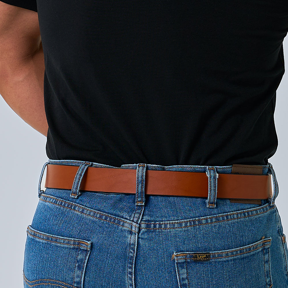 A person is shown from the waist down wearing a black shirt, blue jeans, and The Double Prong Everyday belt by Hanks Belts, standing with their hands behind their back.