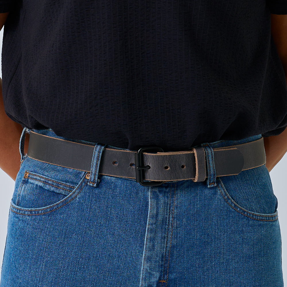 Person wearing a grey leather belt with blue jeans on a light gray background