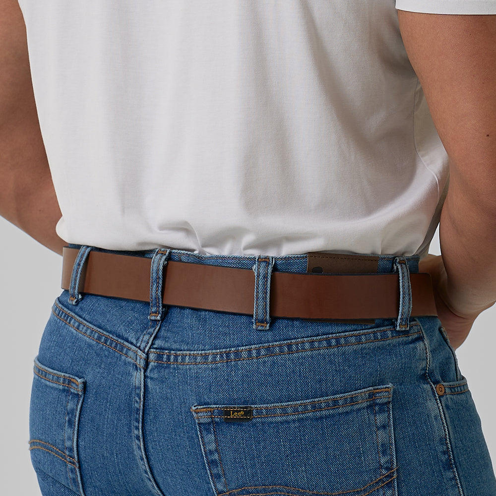 A person wears a white shirt tucked into blue jeans, showcasing the fit and details at the back waist with Hanks Belts&#39; sturdy Gunner belt.