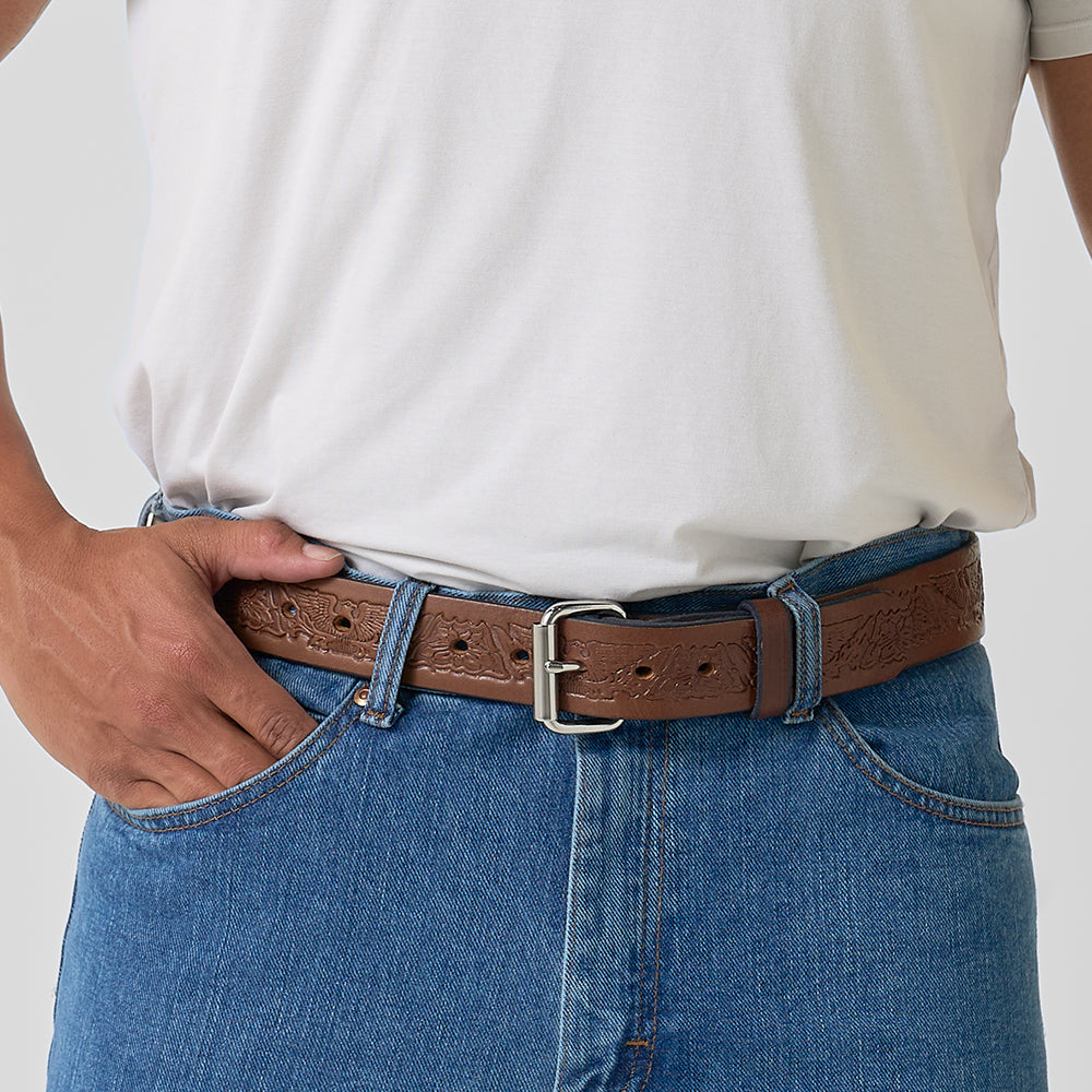 A person stands with one hand in their pocket, wearing a plain white T-shirt, blue jeans, and the Hanks Belts Gunner Eagle brown full-grain leather gun belt.
