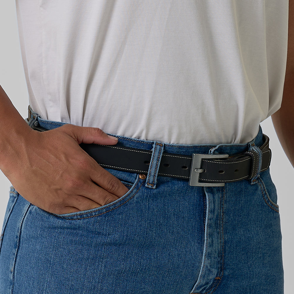 A person wearing a white shirt tucked into blue jeans with The Heritage Bison belt by Hanks Belts, crafted in the USA, resting one hand in the front pocket.