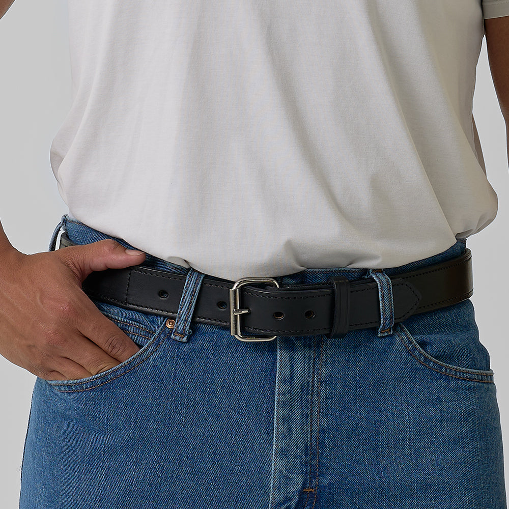 A person wearing a plain white t-shirt tucked into blue jeans with The Kydex Reinforced gun belt from Hanks Belts, standing with one hand resting on their hip.
