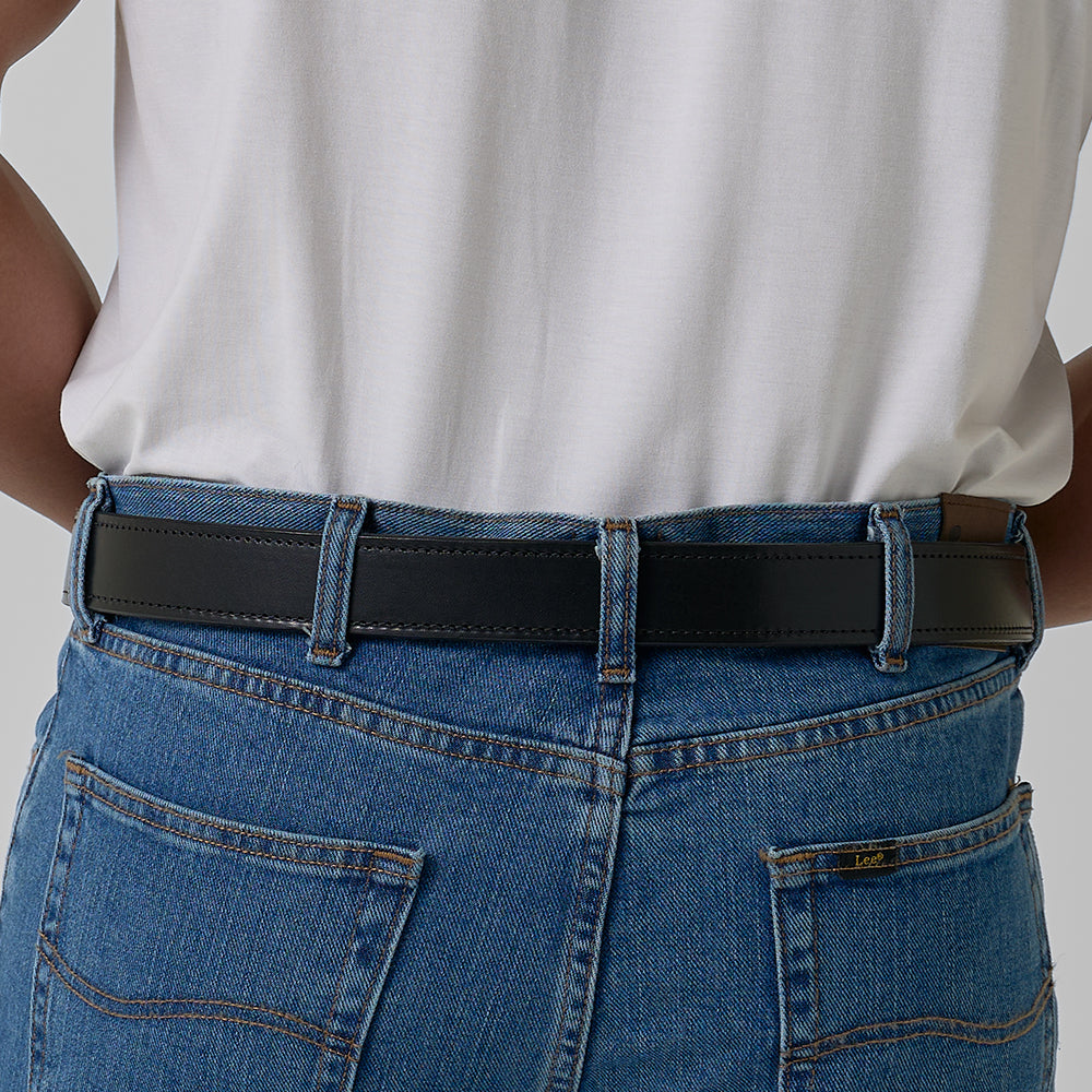 A person is seen from behind wearing blue jeans and a white tucked-in shirt, showing off The Kydex Reinforced by Hanks Belts, a concealed carry belt. Hands rest on hips with jean pockets visible.