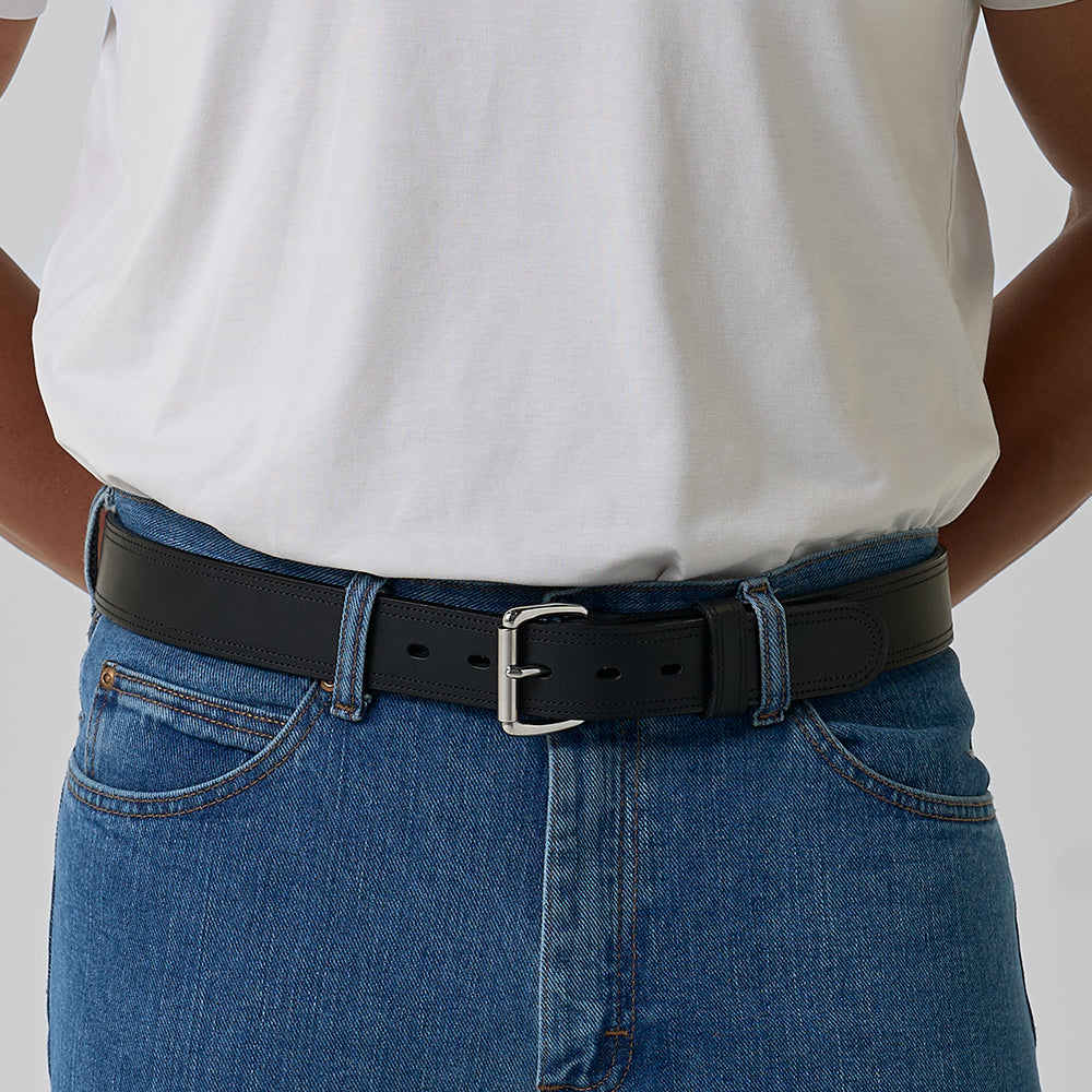 A person wears a plain white t-shirt tucked into blue jeans with The Old World Harness by Hanks Belts, featuring a silver buckle. Their hands are behind their back, showing only the torso and waist.