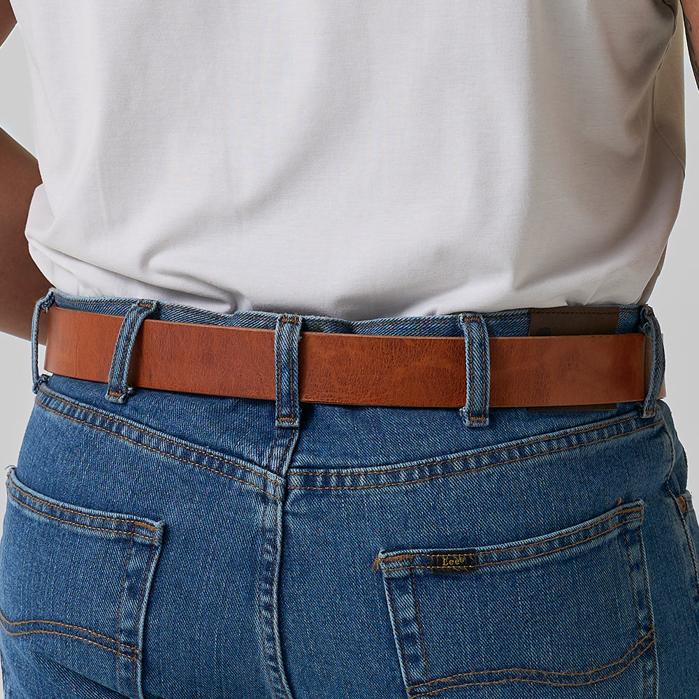 Wearing blue jeans and a tucked-in white shirt, the focus is on The Old World Harness belt from Hanks Belts—crafted from premium USA-tanned Hermann Oak full-grain leather with a visible brand tag. Perfect as a concealed carry belt.