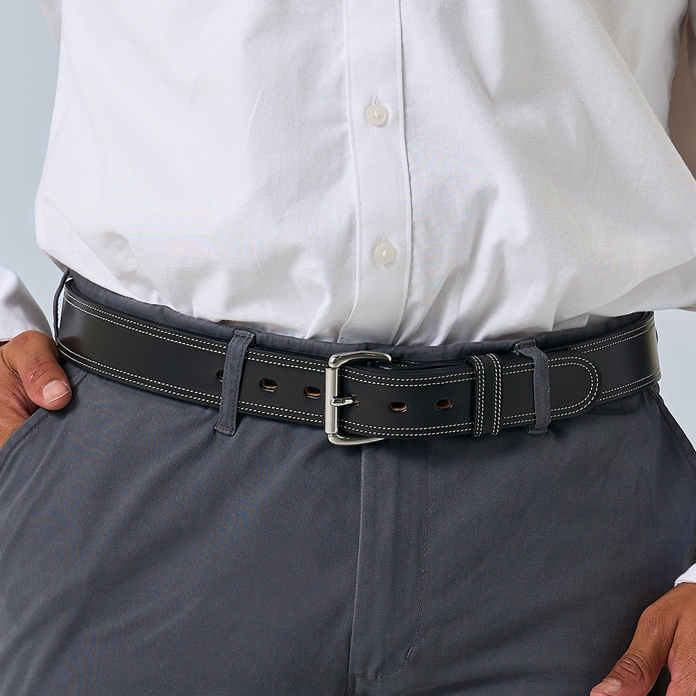 A person wearing a white button-down shirt tucked into gray pants with The Premier Double Layer by Hanks Belts, a vegetable-tanned leather belt featuring white stitching and a silver buckle.