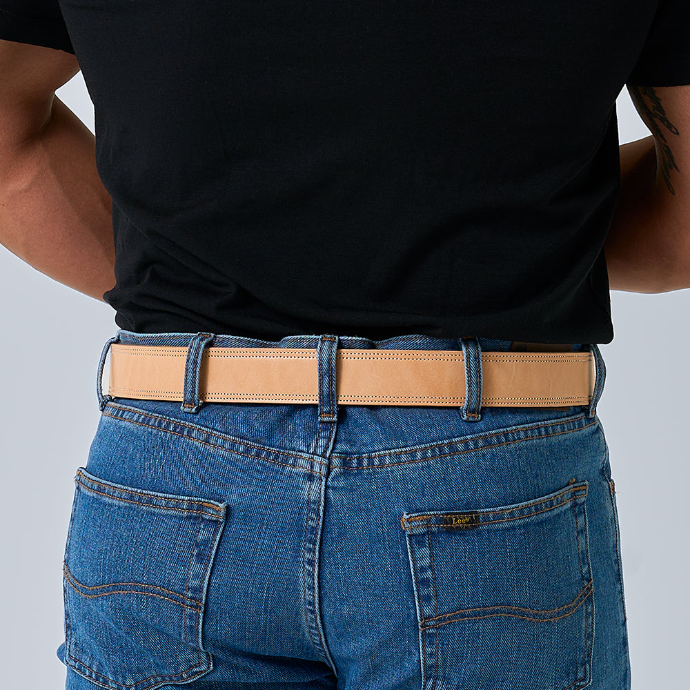 A person in a black shirt tucked into blue jeans, seen from the back, wears Hanks Belts&#39; The Premier Double Layer—a tan English bridle belt crafted from vegetable-tanned leather.