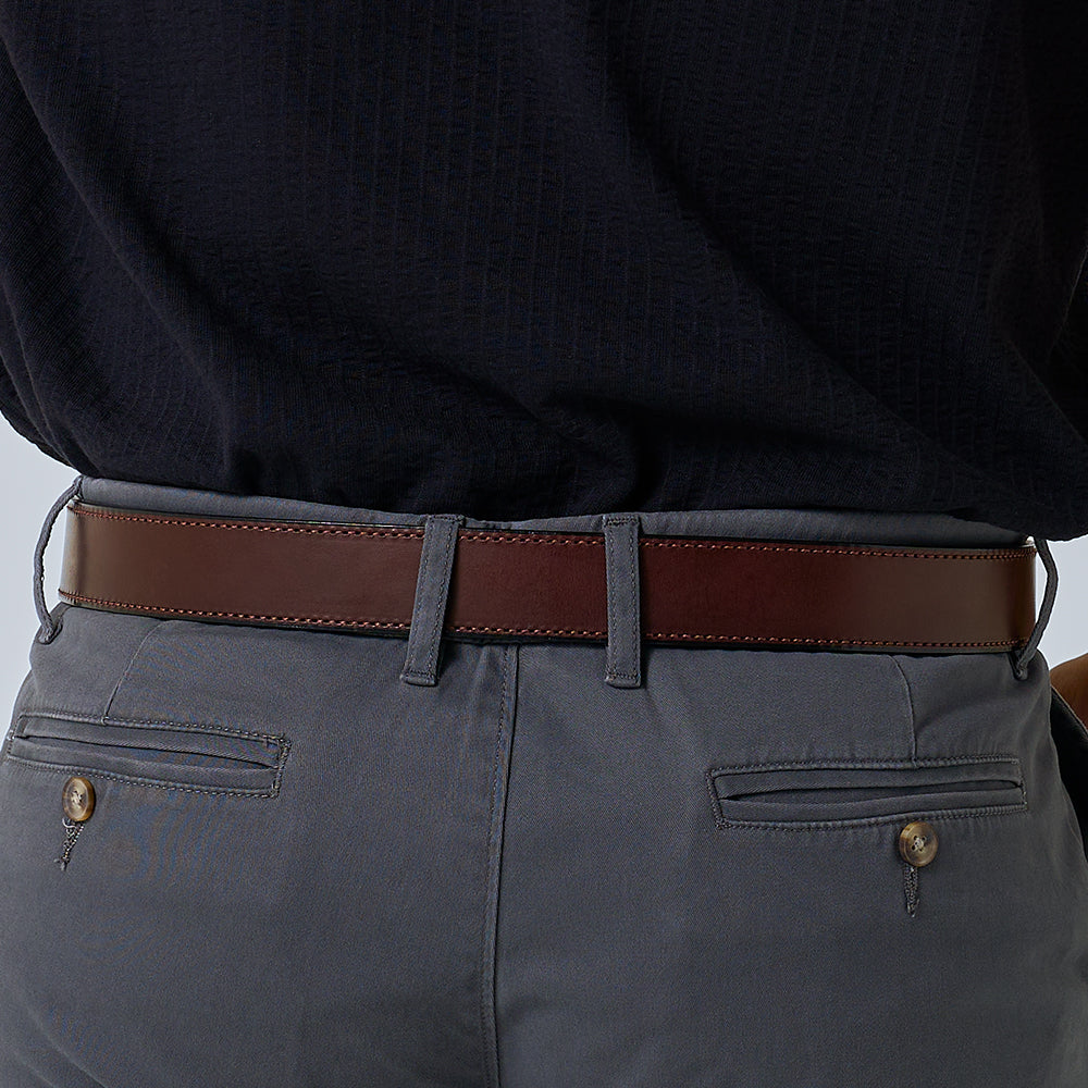 A close-up of a person wearing grey pants, a dark textured shirt tucked in, and The Ranger full grain leather belt by Hanks Belts.