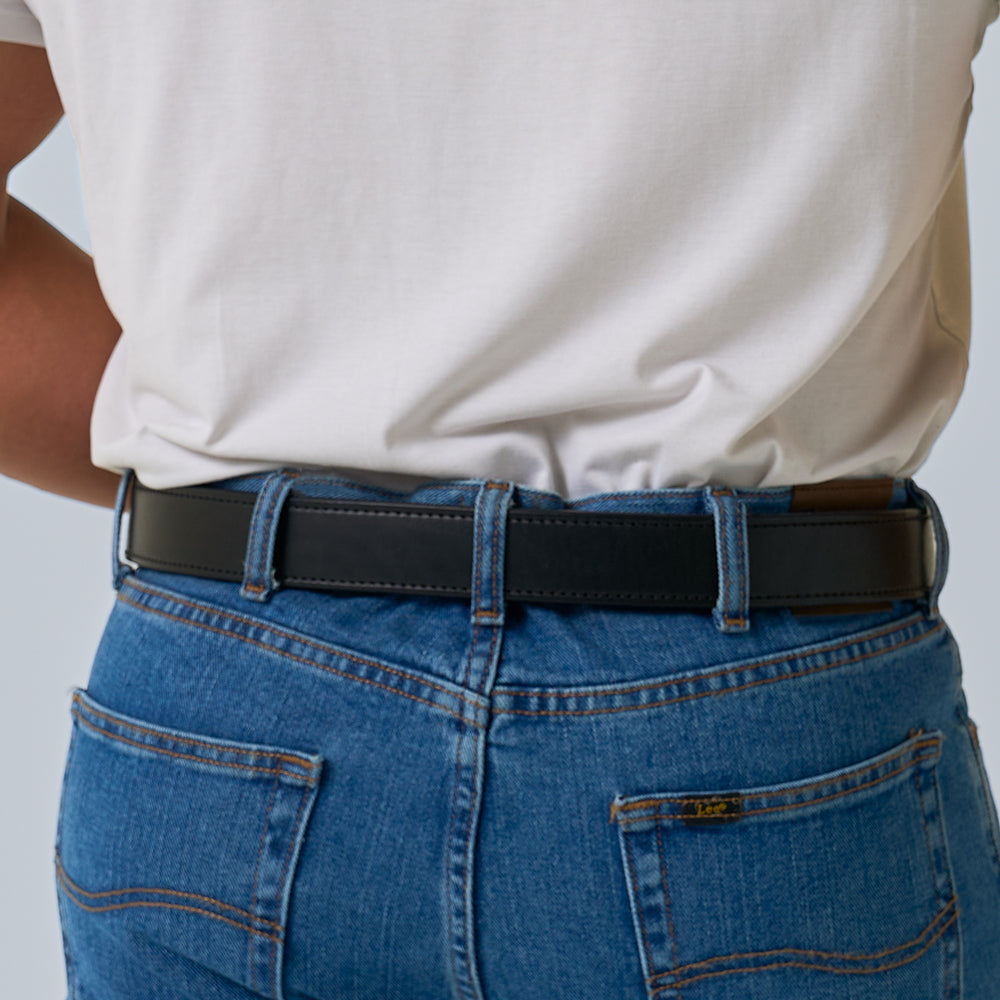 A person is shown from the back, wearing a white T-shirt, blue jeans, and The Steel Core - 1.5&quot; belt by Hanks Belts, with focus on the waist and hips.