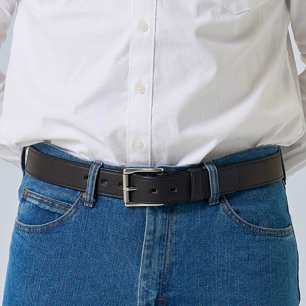 Person wearing a black belt with a white shirt and blue jeans on a light gray background