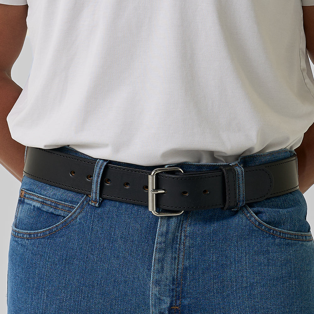A person stands with hands behind their back, wearing a white t-shirt tucked into blue jeans, secured by The Xtreme - 1.75&quot; heavy-duty leather belt from Hanks Belts with a silver buckle.