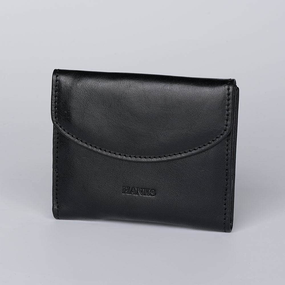 The Adelina Mini Bifold by Hanks Belts is a black leather wallet with a flap closure and "HANKS" embossed on the front, shown against a plain light gray background.