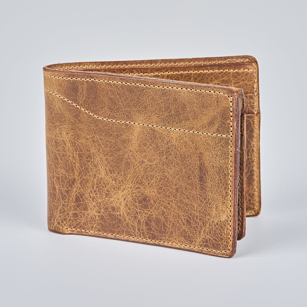 The Champlain Bison Bifold with ID Window by Hanks Belts stands upright on a light gray background, showcasing its weathered brown bison leather texture and closed front and side. Made in the USA.