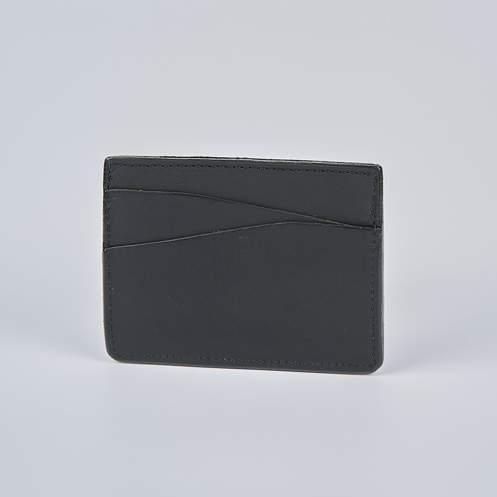The Cumberland Bison Card Holder by Hanks Belts is a minimalist USA-made black leather card holder with subtle stitching and two curved card slots, shown upright against a plain light gray background.