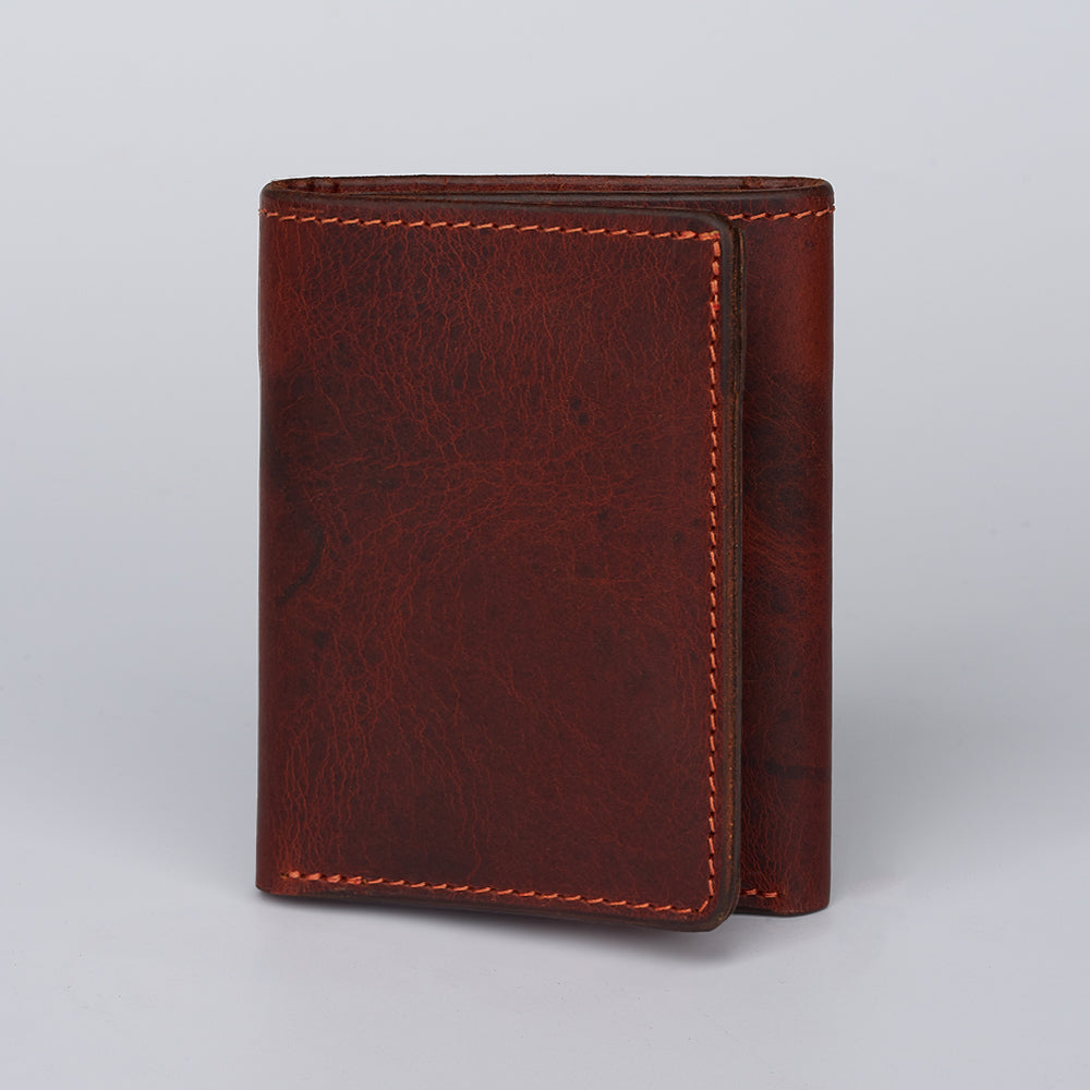 The Hanks Belts Erie Premium Bison Trifold, made in the USA, stands upright closed on a light gray background. Its brown bison leather, visible stitching, and textured surface highlight its premium craftsmanship and neat edges.
