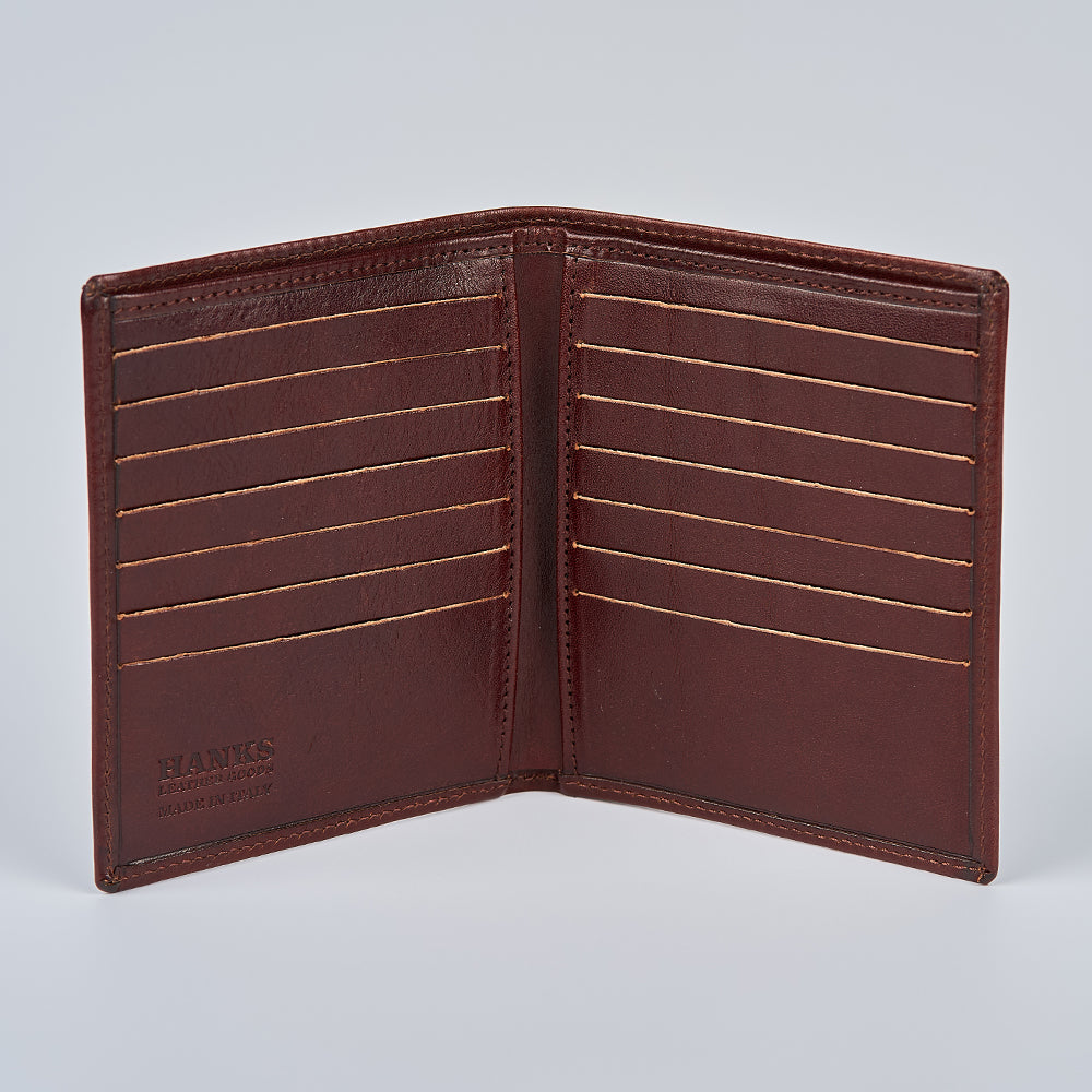 The Hanks Belts Iseo Italian Hipster Bifold wallet in brown full-grain leather is open, displaying multiple card slots, smooth interior with visible stitching, and "HANKS" and "MADE IN USA" embossed on the lower left against a light gray background.