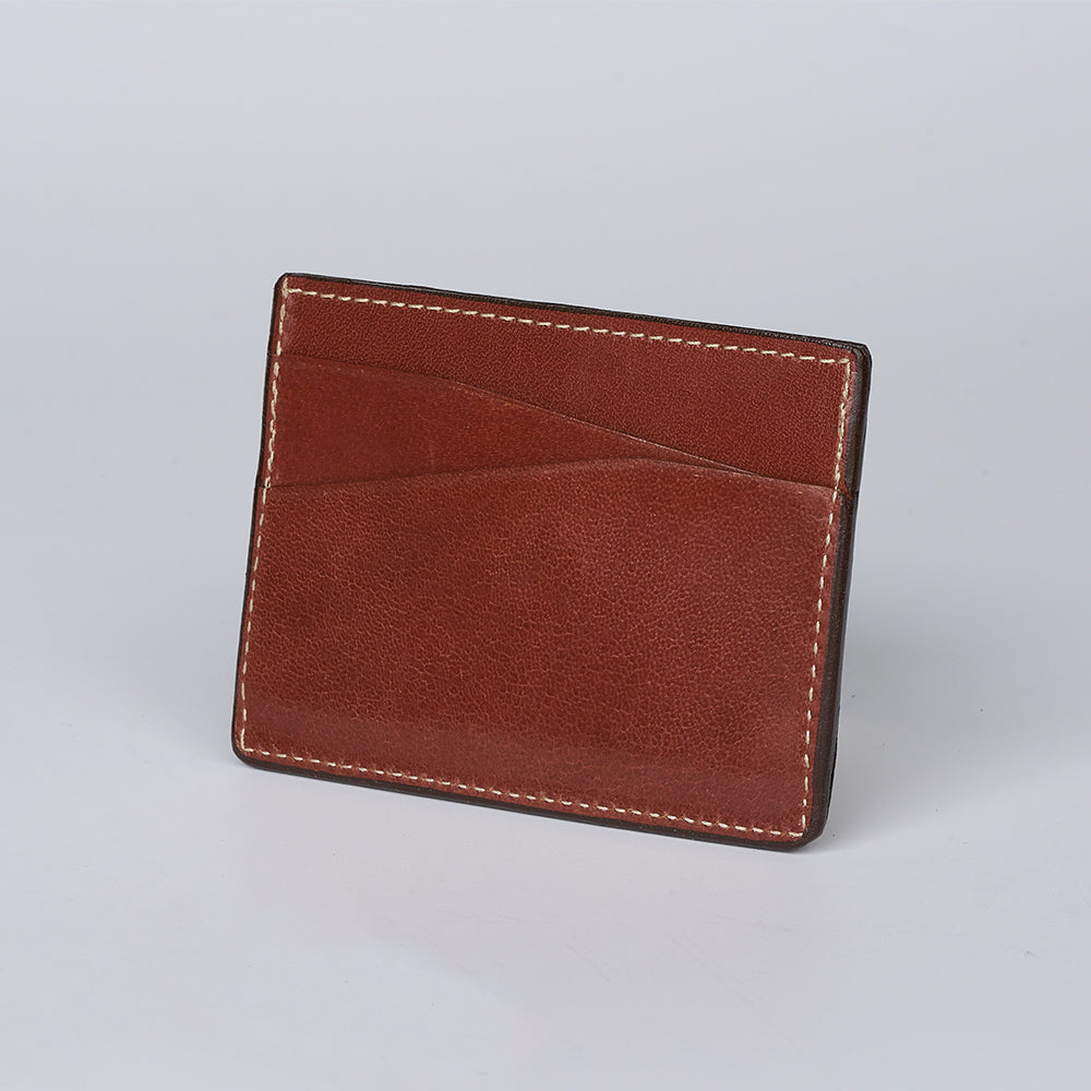The Monroe Goatskin Card Holder by Hanks Belts is a brown leather minimalist wallet with visible stitching and two angled card slots, displayed upright on a light gray background.