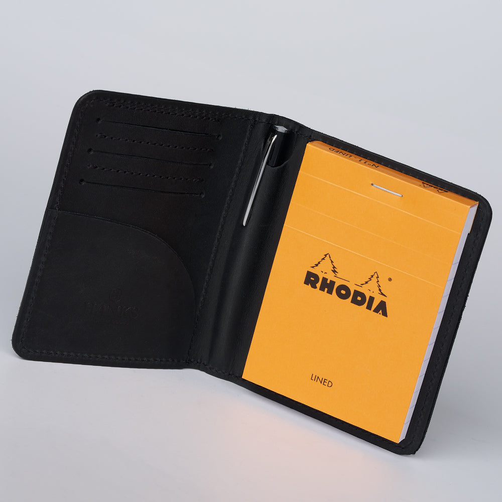 The Hanks Belts Notesman and Credit Card Wallet is open, showing card slots on the left and a bright orange Rhodia notepad with pen on the right, all set against a plain light background.
