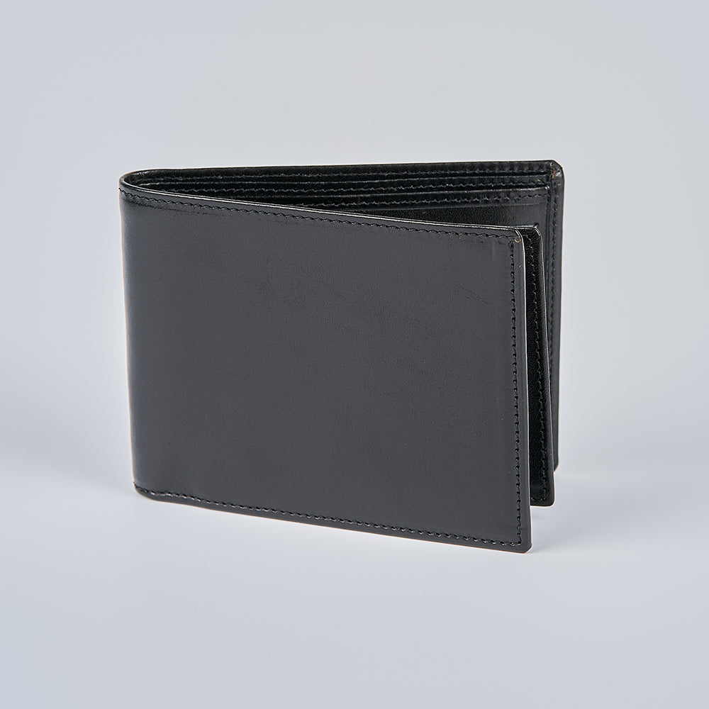 The Hanks Belts Orta Italian Bifold with ID Window stands upright, closed, on a plain light gray background, showing off its smooth, polished leather surface.