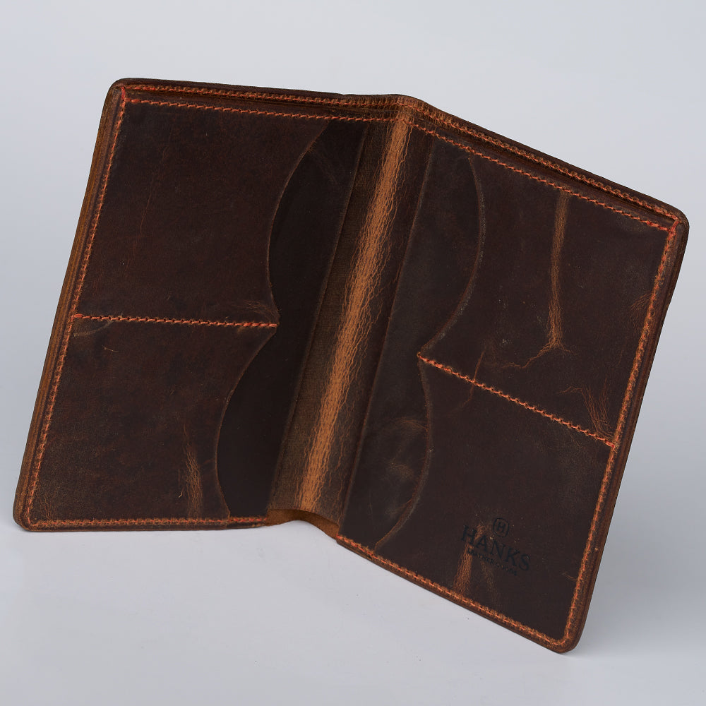 An open brown Passport Case Wallet by Hanks Belts, crafted from North American Steerhide with visible stitching and multiple interior pockets. &quot;HANKS&quot; is embossed on the lower right, reflecting its USA-made quality and slightly worn texture.