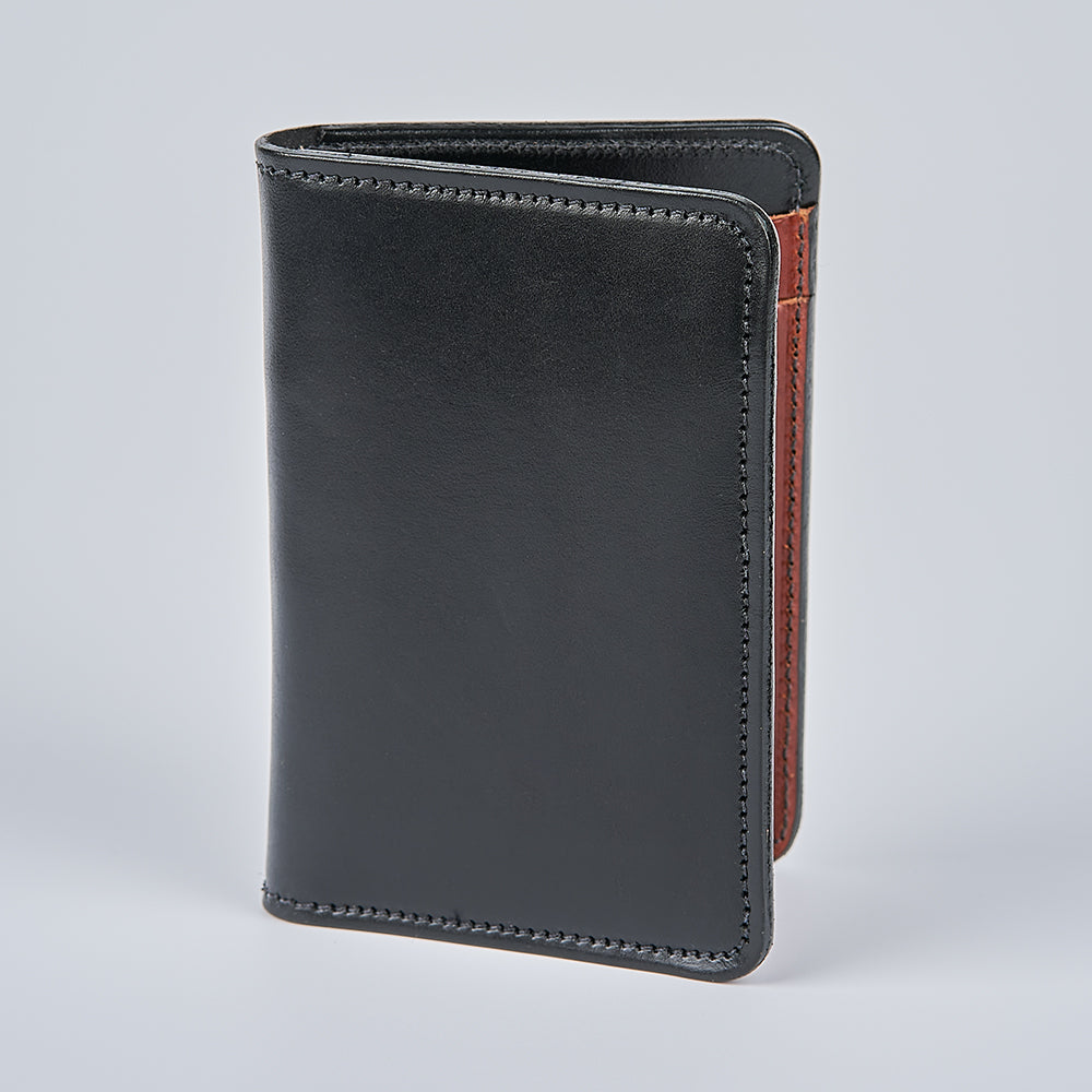 The Hanks Belts Superior Front Pocket Bifold, handcrafted from English Bridle leather, stands upright on a light gray background, highlighting edge stitching and a glimpse of its brown interior lining.