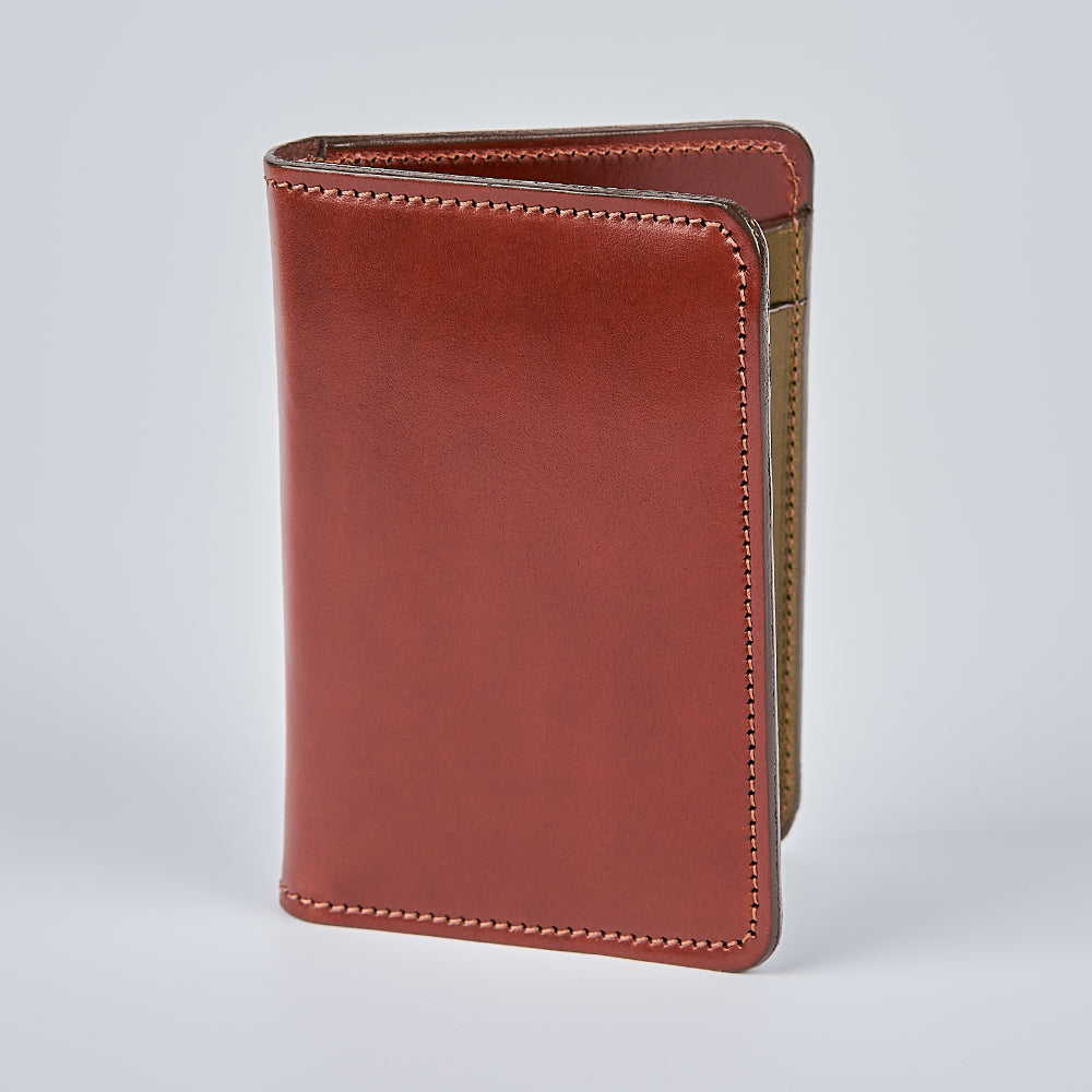 The Hanks Belts Superior Front Pocket Bifold, crafted from English Bridle Leather, stands upright on a light gray surface with visible edge stitching and a slightly open side showing its interior.
