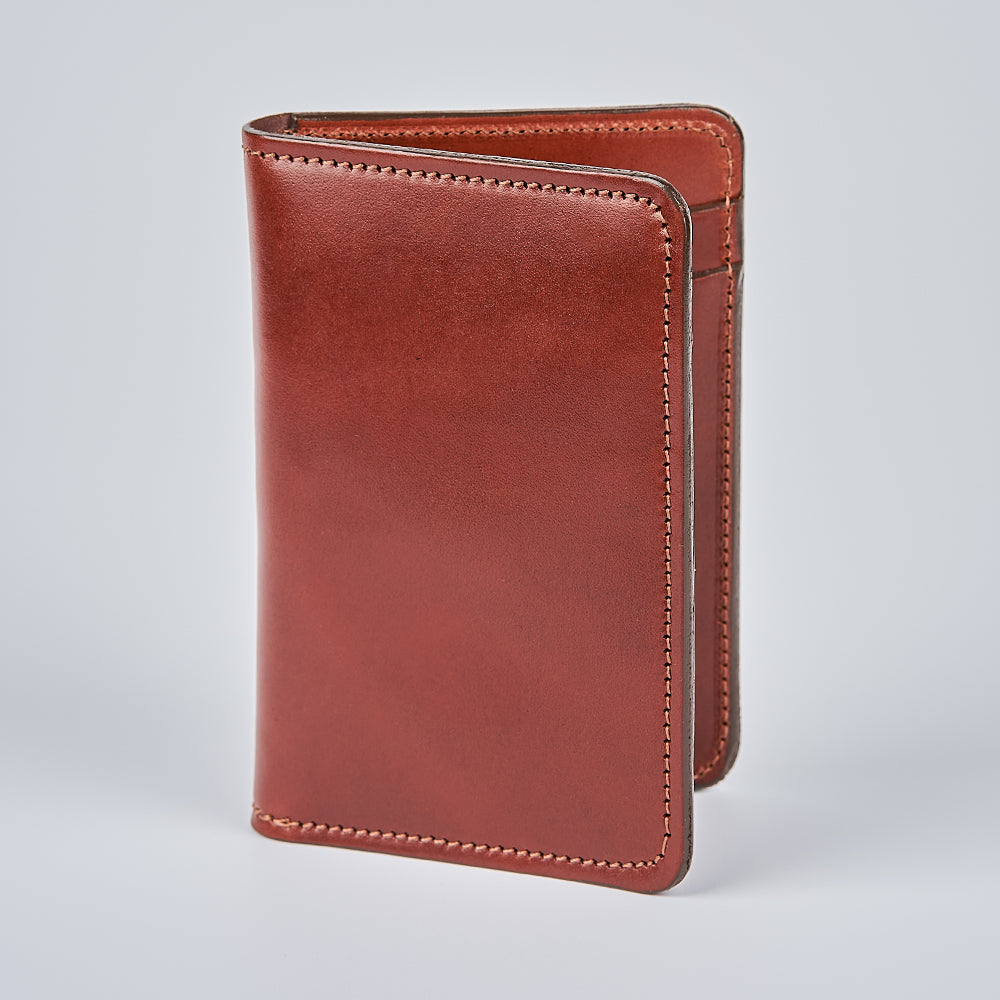 The Hanks Belts Superior Front Pocket Bifold wallet, crafted in brown English Bridle leather, stands upright on a light gray surface with its detailed edge stitching clearly visible.