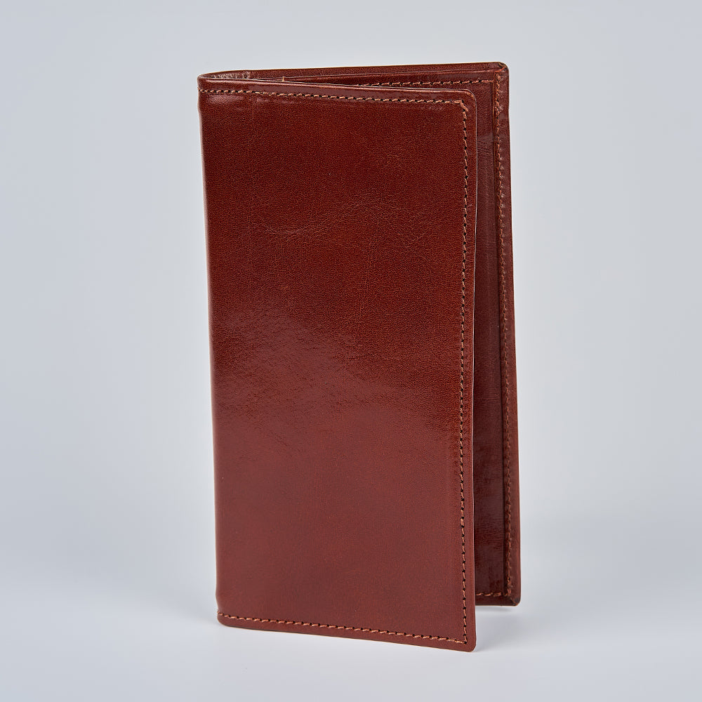The Vico Italian Breast Pocket Bifold by Hanks Belts, a tall and slim leather wallet with visible edge stitching, stands upright and closed on a plain light gray background.