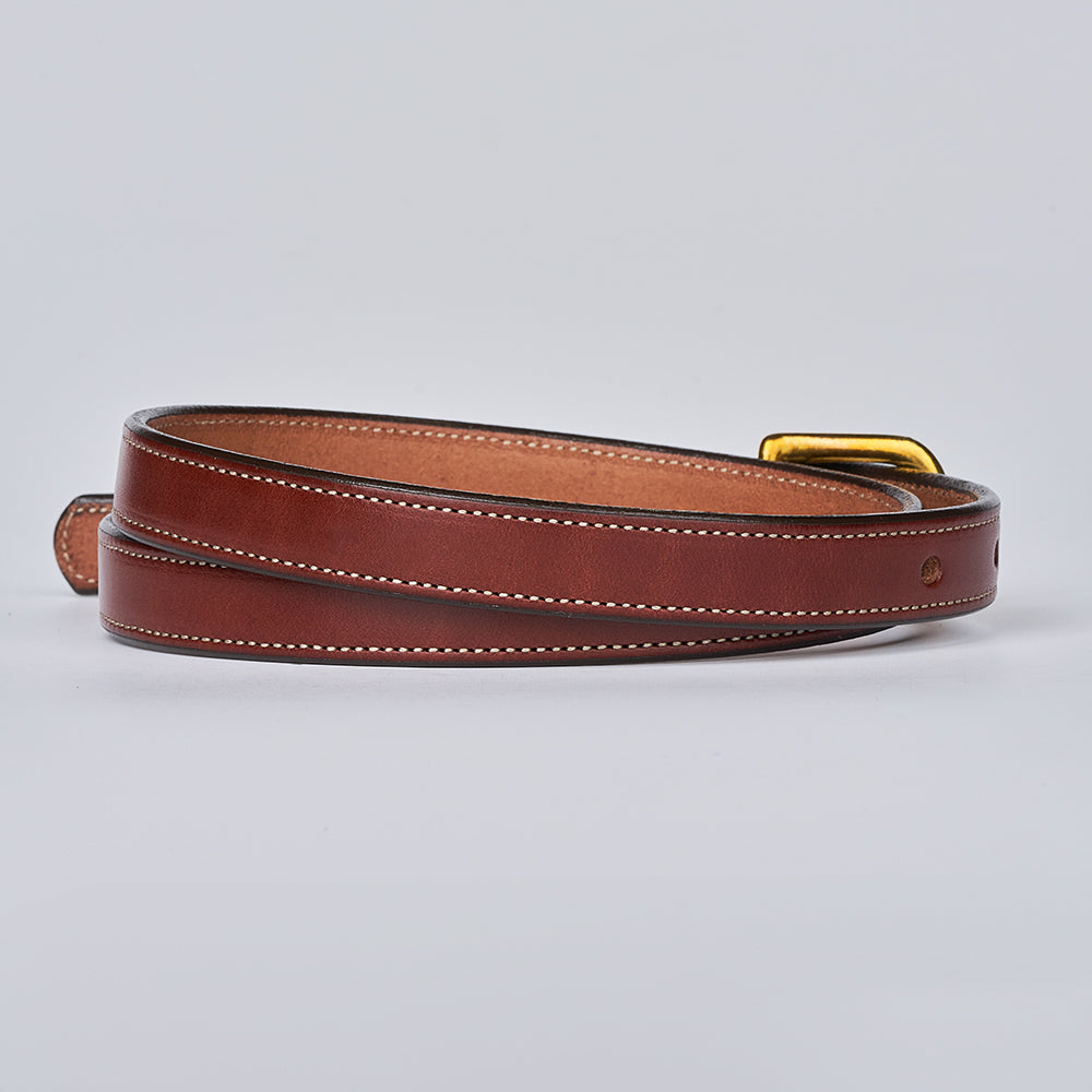 The Dixie by Hanks Belts—a brown English Bridle leather women&#39;s belt with white stitching and a gold buckle—coiled on a light background. A stylish accessory for any wardrobe.