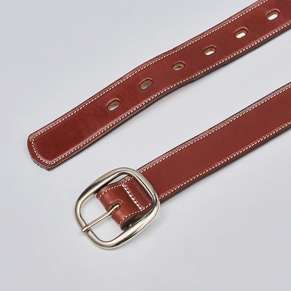 The Eloise by Hanks Belts, a women&#39;s vegetable-tanned brown leather belt with white stitching and a silver buckle, made in the USA, is laid flat on a light gray surface.