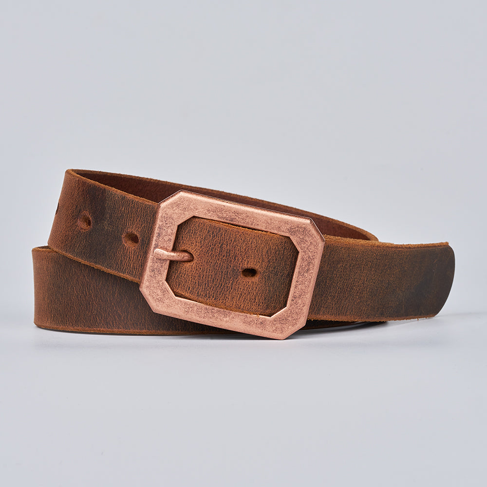 The Lainey by Hanks Belts, a brown women&#39;s leather belt with an angular bronze-colored buckle, is coiled neatly on a plain light gray background.