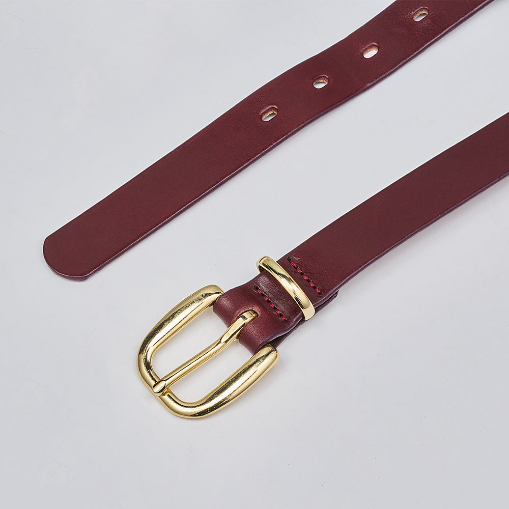 The Poppy by Hanks Belts is a burgundy women&#39;s leather belt with a brass buckle, shown on a light gray background. This statement piece offers multiple holes for easy adjustment.