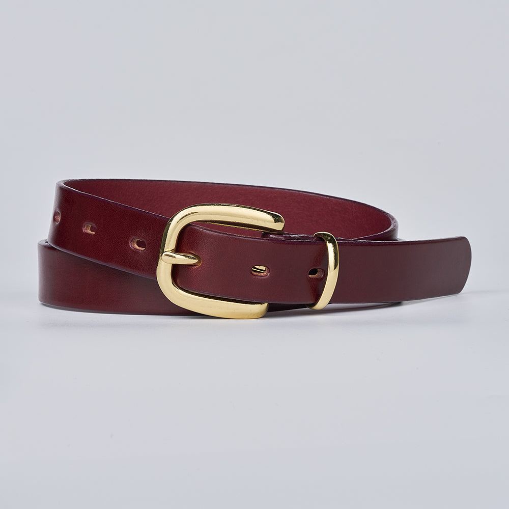 The Poppy by Hanks Belts is a rolled-up, burgundy women&#39;s leather belt with a shiny brass buckle, displayed on a plain light gray background.