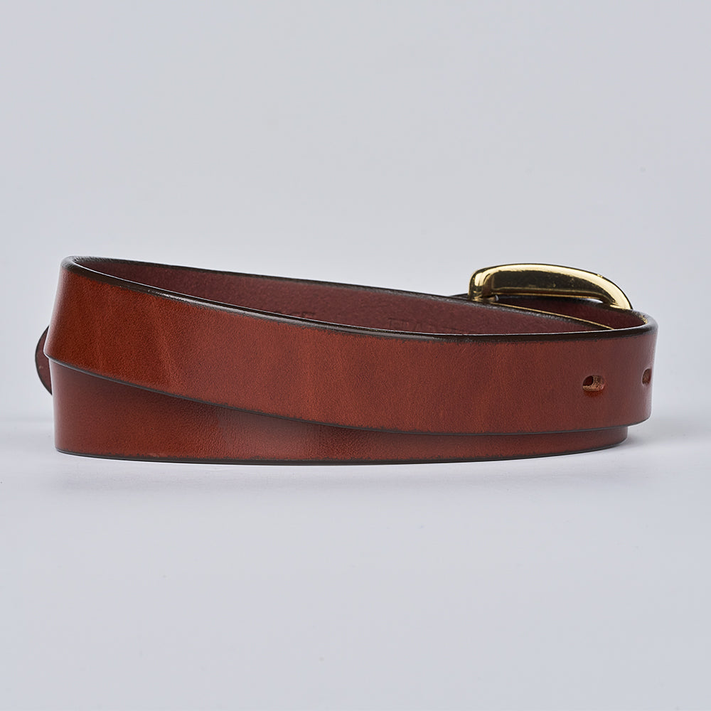The Poppy by Hanks Belts, an oak leather women&#39;s statement belt with a shiny gold buckle, is shown coiled in a loose loop against a light gray background.