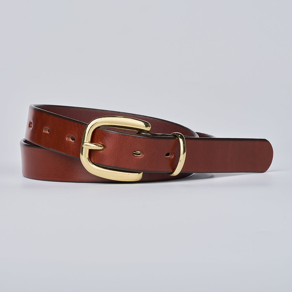 The Poppy by Hanks Belts, an oak leather belt with a shiny brass buckle, is coiled neatly on a plain light gray background.