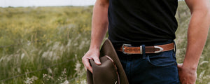 Person holding a brown leather Hat in a field wearing Mens Dakota Belt in Brown