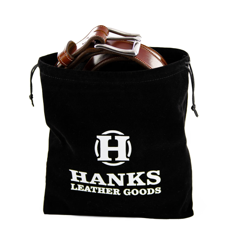 The Hanks Premium Velvet Gift Bag by Hanks Belts, with a double cord drawstring and logo, contains brown leather belts with shiny silver buckles.