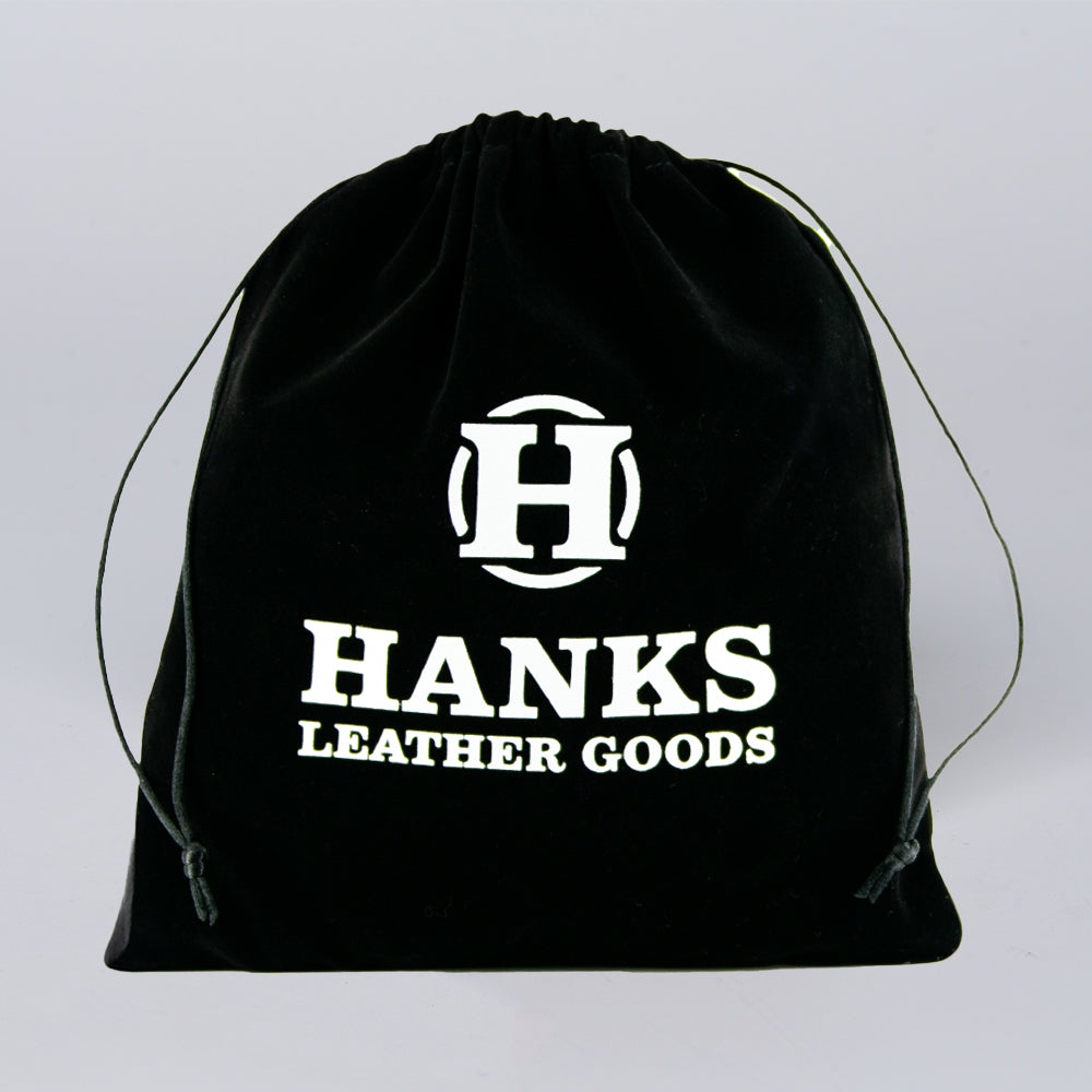 The Hanks Premium Velvet Gift Bag by Hanks Belts is a black drawstring bag with a large white "H" logo and "HANKS LEATHER GOODS" on the front, perfect for storing belts. The bag is shown upright against a plain light background.