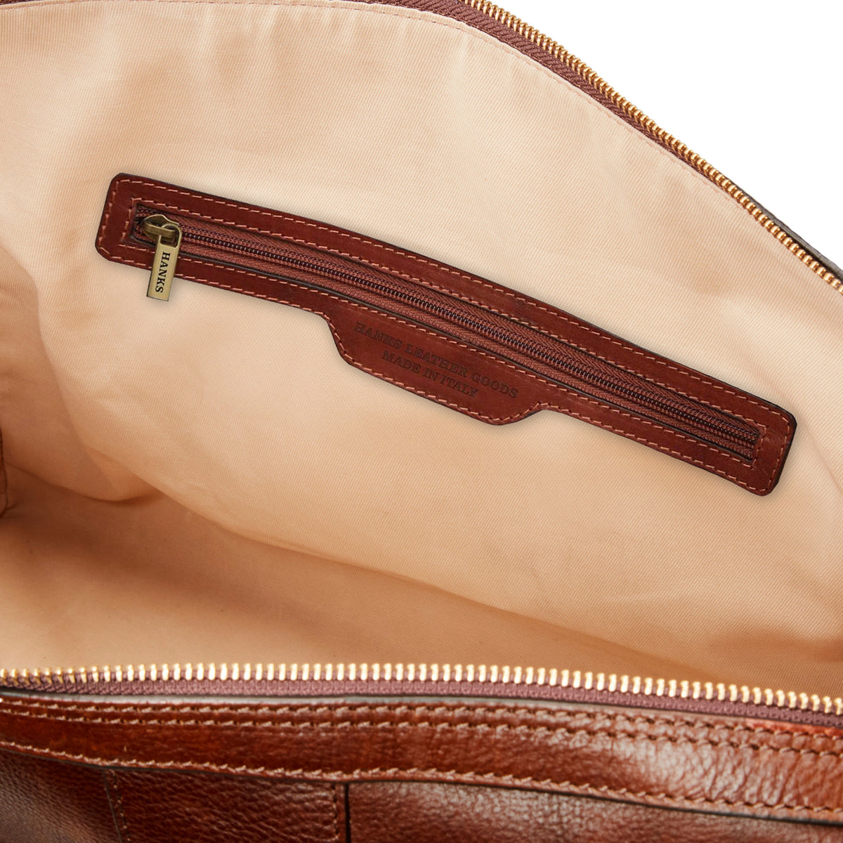 Inside the Getaway Duffel With Luggage Sleeve by Hanks Belts, you&#39;ll discover a luxurious brown Italian leather exterior paired with a tan lining. The interior includes a zippered pocket with a pull tab and proudly displays a &quot;Made in Italy&quot; label. Its spacious main compartment makes it an ideal option for carry-on-friendly luggage.