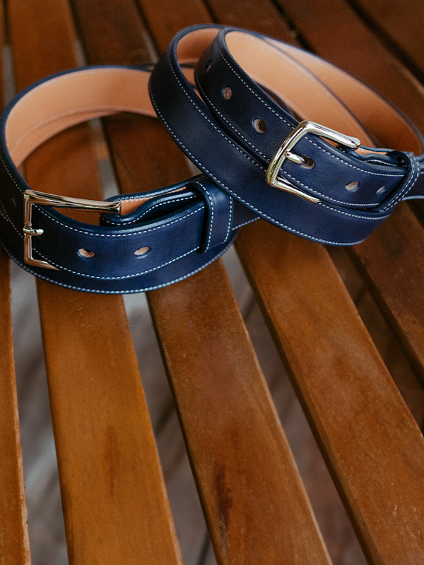 Two leather belts, both Navy blue, on a wooden surface.