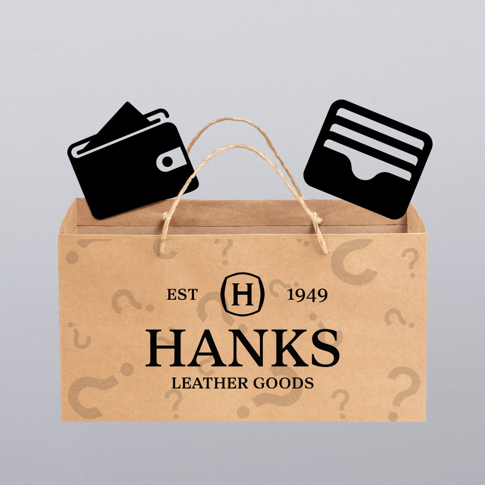A brown shopping bag labeled &quot;Hanks Belts&quot; shows simple black wallet and cardholder icons peeking out, hinting at the Less-Than-Perfect Mystery Bag: 2 Wallets Per Bag, set against a light gray background.