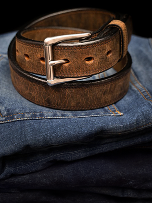 Brown leather belt with a silver buckle on blue jeans