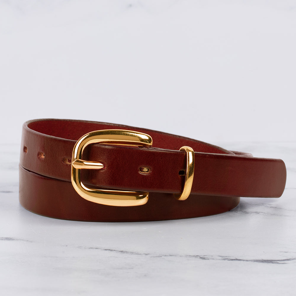 The Poppy - 1&quot; by Hanks Belts, crafted from premium leather with a shiny gold buckle, is neatly coiled on a white marble surface—a versatile accessory for any wardrobe.