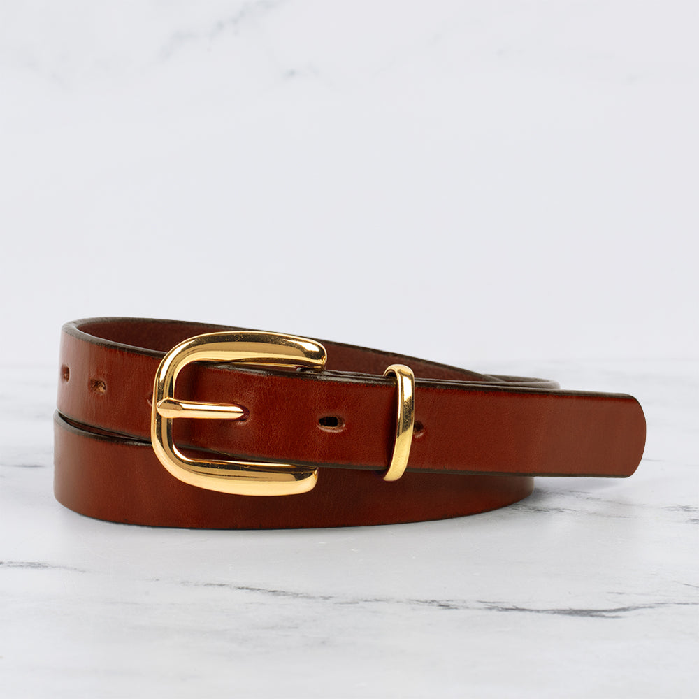 The Poppy - 1&quot; by Hanks Belts is a premium leather belt with a shiny gold buckle, elegantly coiled on a white marble surface.
