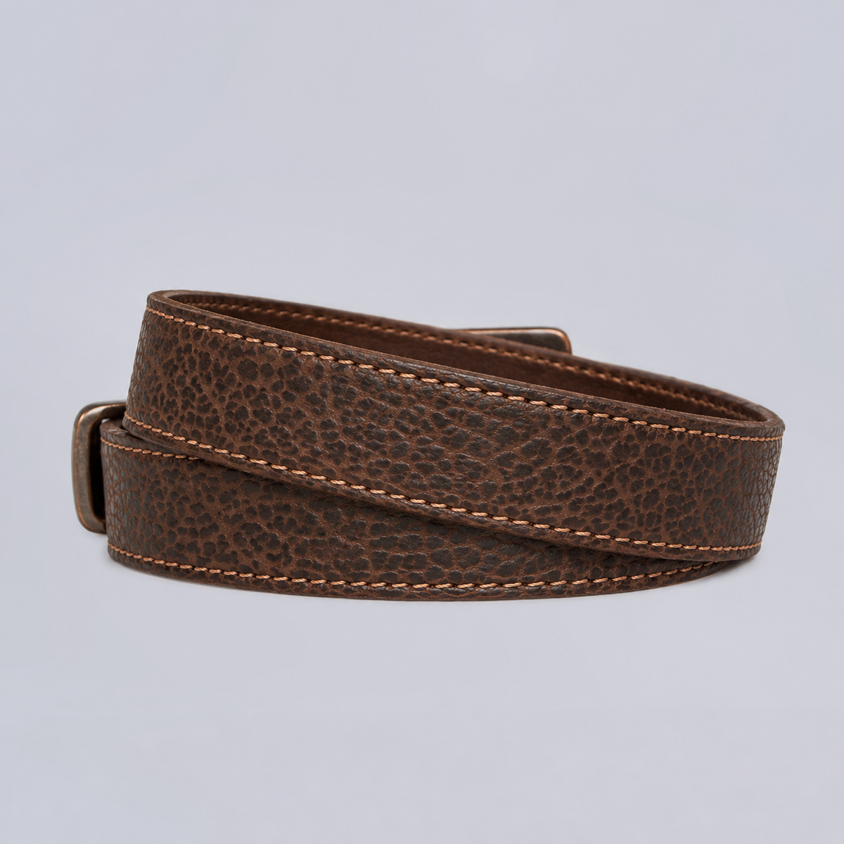 The Yellowstone - 1.25″ brown leather belt with a textured surface and stitched edges, coiled against a neutral background.