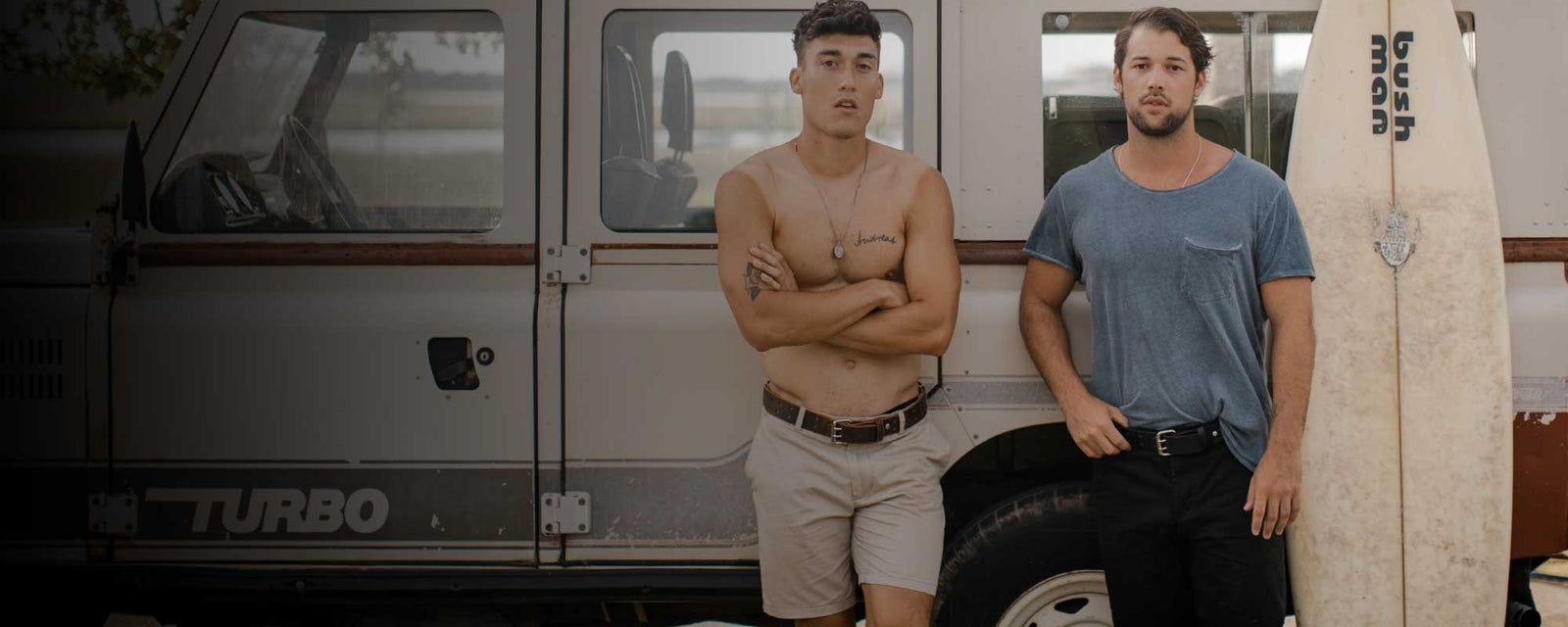 2 Young men leaning on 4wheeldrive truck with a surfboard wearing Hanks Belts in the summertime