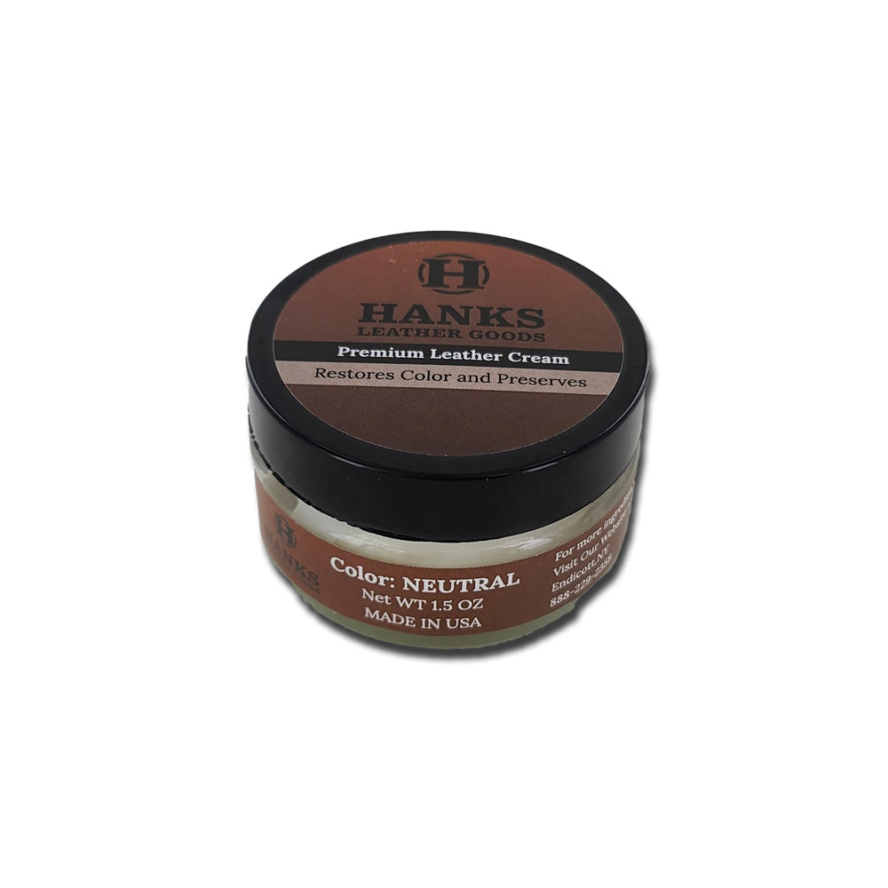 A small jar of Hanks Belts&#39; Premium Leather Cream and Color Restoration is adorned with a brown label on the lid. The text reads, &quot;Restores Color and Preserves,&quot; and &quot;Color: Neutral, Net WT 1.5 oz, Made in USA.&quot; Designed for leather products, this cream promises to restore and refinish your treasured items. The jar features a black screw-on lid.