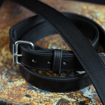 A close-up of a Hanks Belts Kydex Reinforced CCW Belt - 1.5" with a silver buckle, coiled and laid flat on a textured, rust-colored surface. The belt features a smooth finish with visible stitching along the edges.